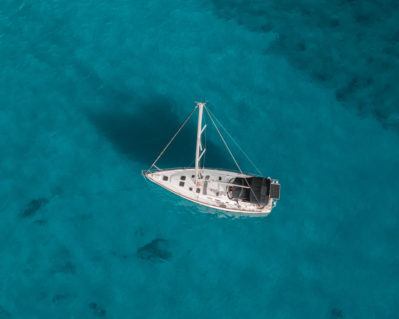 Aerial overhead view of a white sailboat anchored on clear turquoise Hawaii water