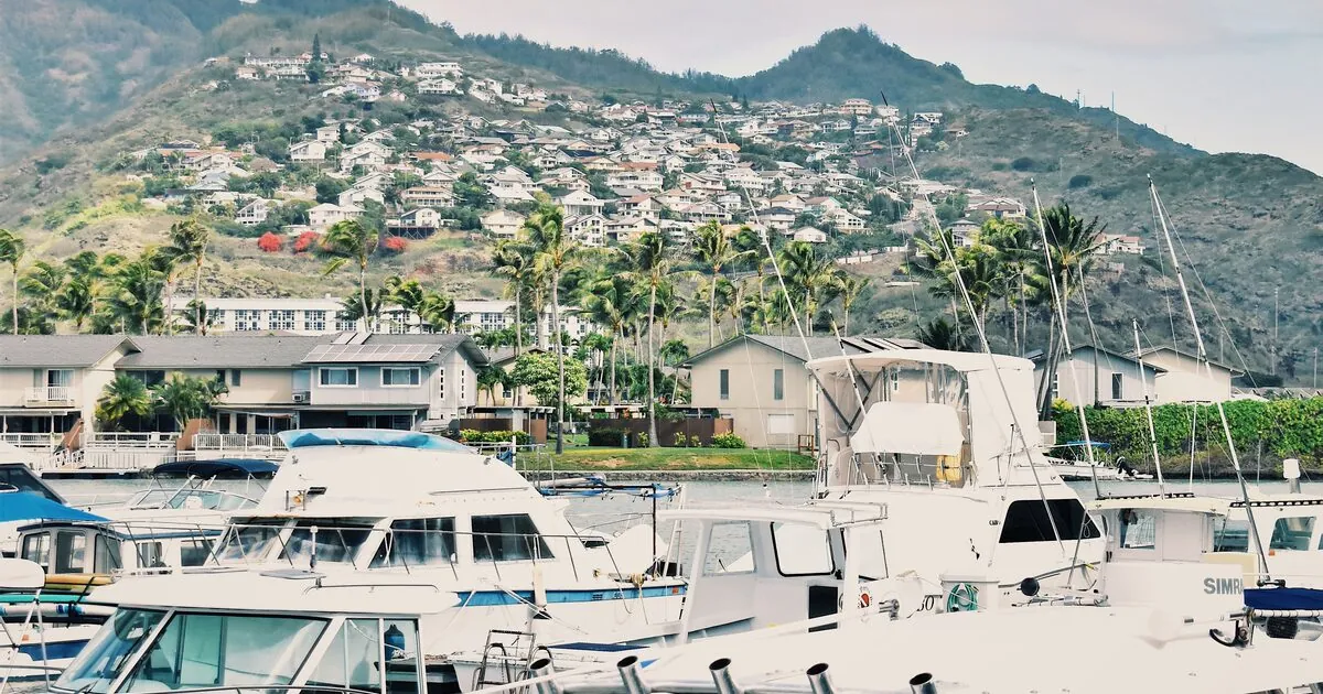 Powerboats and sportfishers docked in an Oahu marina below green hillside homes, Hawaii