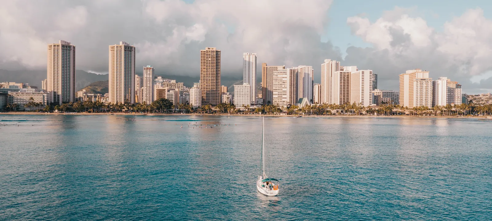 A sailboat anchored on calm blue water off Waikiki with the Honolulu skyline behind, Oahu