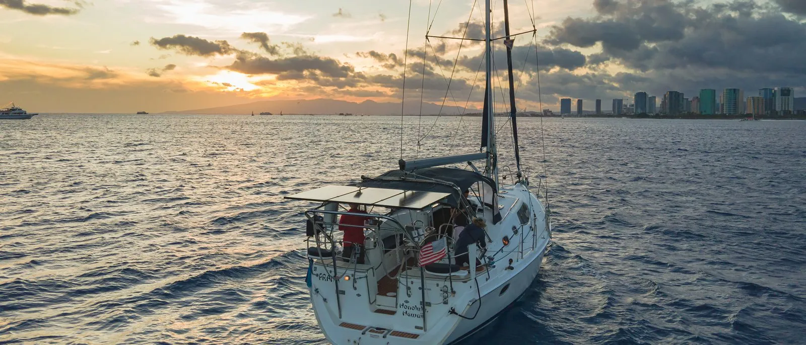 Aerial drone view of the Hunter 45 sailboat Praha underway off Honolulu at sunset, full boat with the Waikiki skyline behind