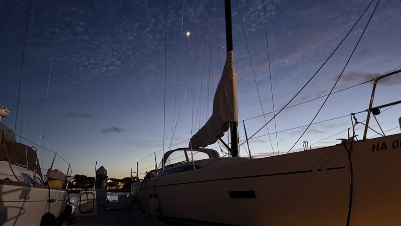 A sailboat tied up in its slip at dusk under a crescent moon at an Oahu marina, Honolulu, Hawaii