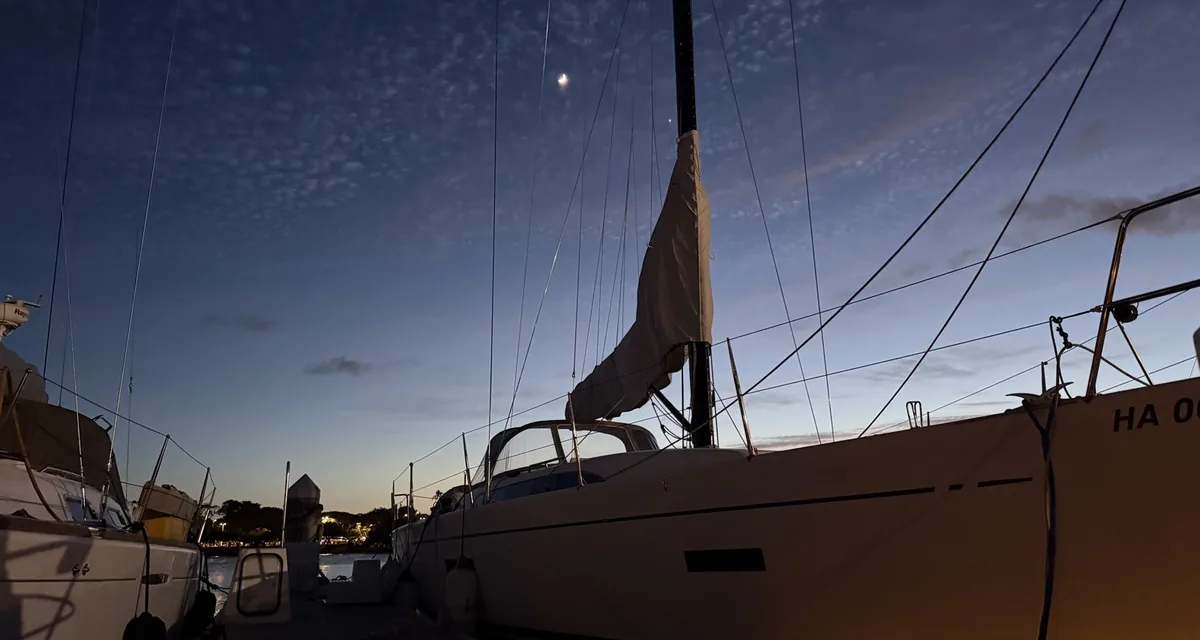 A sailboat tied up in its slip at dusk under a crescent moon at an Oahu marina, Honolulu, Hawaii