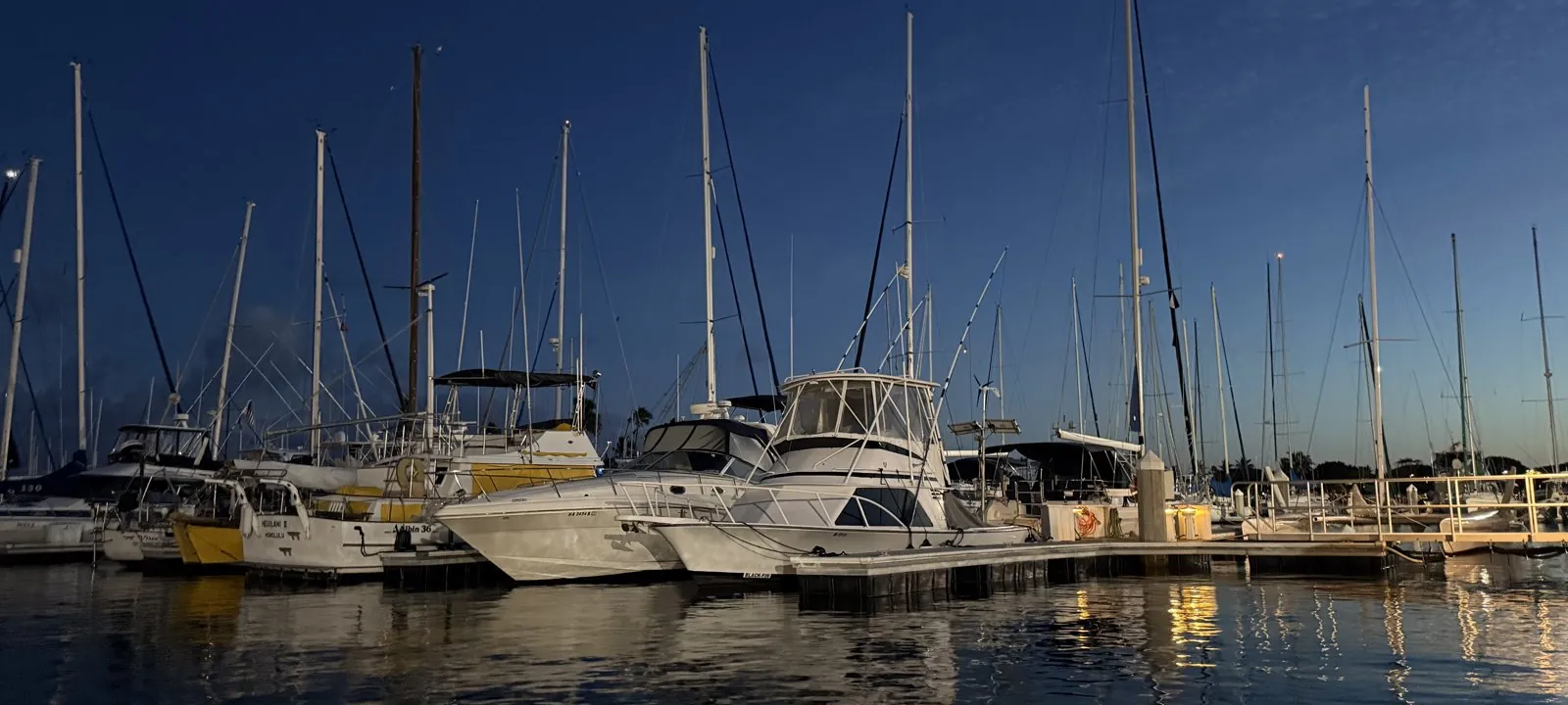 Sailboats and a sportfisher moored at the Ala Wai Boat Harbor at dusk, one transom marked Honolulu, Oahu, Hawaii