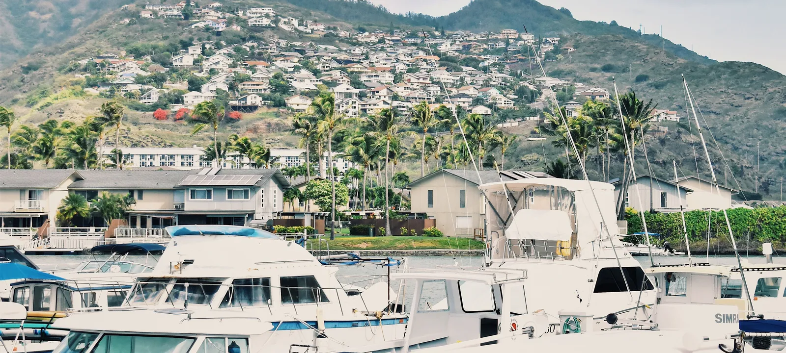 Powerboats docked in an Oahu marina with a green Hawaii Kai hillside and homes behind