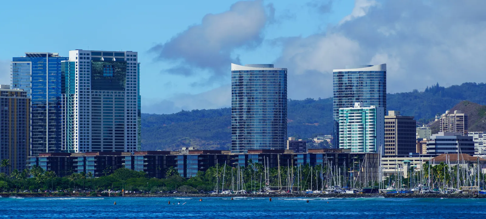 Sailboat masts in an Oahu harbor with the Honolulu high-rise skyline and mountains behind